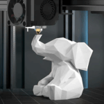 Weißes, niedrigpolyederes Elefantenmodell sitzt auf der Bauplatte eines 3D-Druckers, während der Extruder direkt über seinem erhobenen Rüssel positioniert ist.