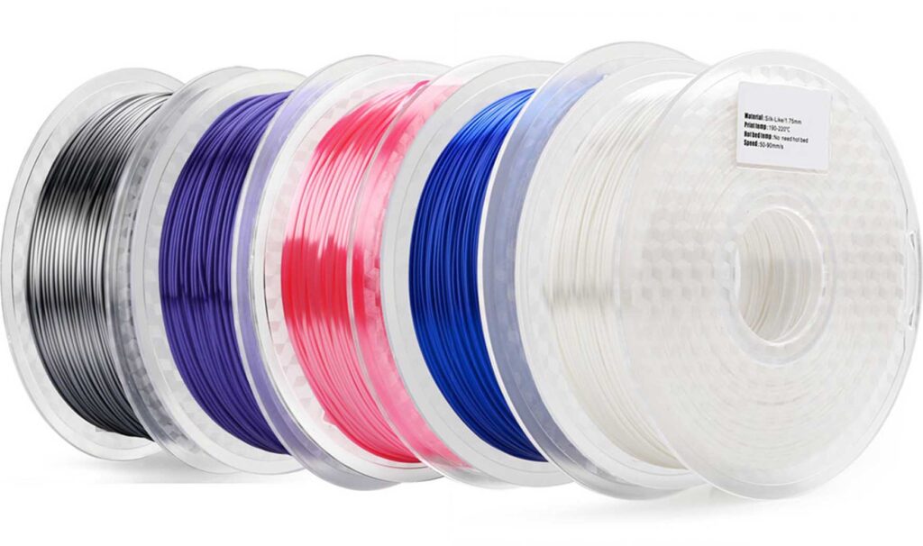 Mehrere durchsichtige Kunststoffspulen mit glänzendem 3D-Druck-Filament in Schwarz, Violett, Pink, Blau und Weiß, halb überlappend und schräg nebeneinander angeordnet.