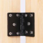 Schwarzes Türscharnier mit je vier silbernen Schrauben, montiert zwischen zwei hellen Holzplatten mit sichtbarer schmaler weißer Fuge in der Mitte.