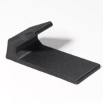 Schwarzes, keilförmiges Kunststoffteil mit texturierter flacher Basis und einer nach oben gebogenen, abgerundeten Lasche, auf weißem Hintergrund mit Schatten.