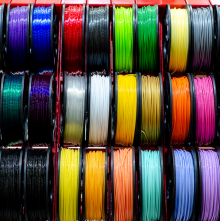 Ordentlich angeordnete Spulen bunten 3D-Druck-Filaments in mehreren Reihen und kräftigen Farben, jede Rolle zeigt glänzenden Faden.